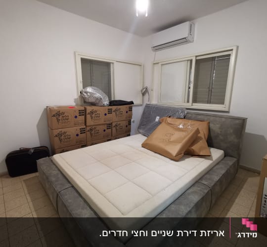 חדר שינה עם קופסאות קרטון ומיטה אפורה